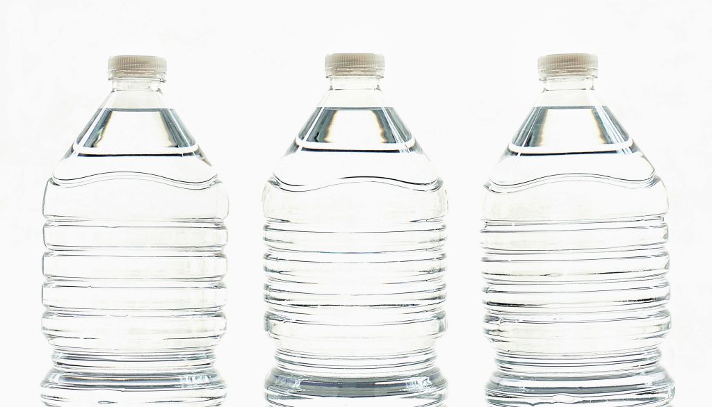 Three clear plastic bottles filled with water, standing side by side.